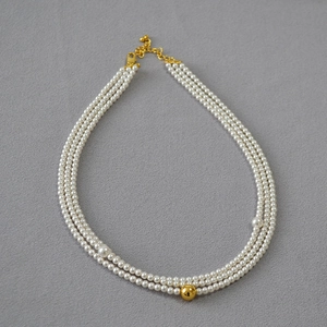 Detailed view of triple-strand pearl necklace with central gold bead on grey fabric
