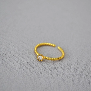 Macro shot of gold-plated twisted brass ring featuring a brilliant zircon stone setting