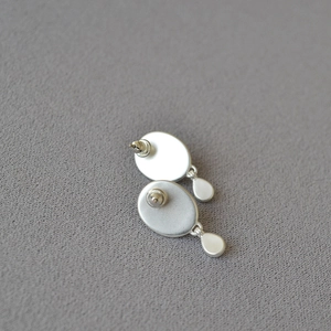 Detail of silver drop earrings with matte brushed finish on a textured grey background