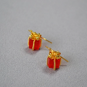 Festive red cube gift box earrings with golden ribbon detail on grey fabric background