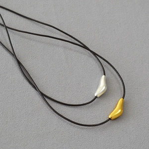 Close-up of minimalist brass bird pendants in gold and silver on adjustable leather cords