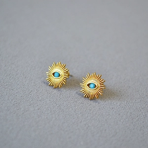 Macro detail of gold-plated sunburst earrings with turquoise evil eye center stone