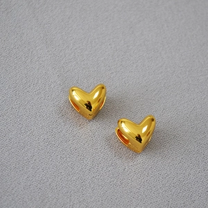 Boucles d'oreilles cœur minimalistes dorées polies sur fond gris avec texture