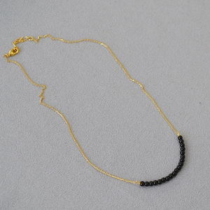 Close-up of a delicate gold chain necklace featuring polished black agate beads and clasp
