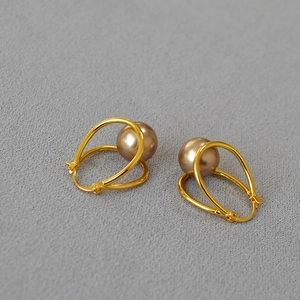 Detail of gold-plated geometric earrings with champagne pearl on a textured surface