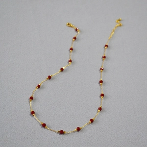 Detailed shot of a brass gold-plated necklace with red faceted cinnabar beads and lobster clasp