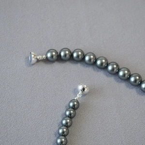Dark grey faux Tahitian pearl necklace with silver magnetic clasp on grey textured base