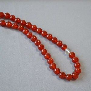Close-up of red agate beaded necklace with clear crystal accent on grey fabric background