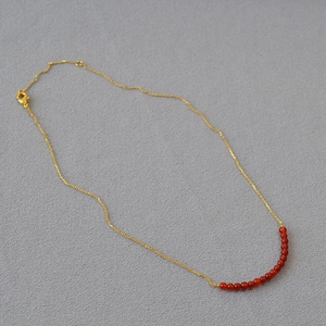 Detailed close-up of minimalist gold necklace with 16 red agate beads and lobster clasp