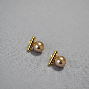 Détail de boucles d'oreilles barre dorée avec perles lisses sur un fond gris neutre