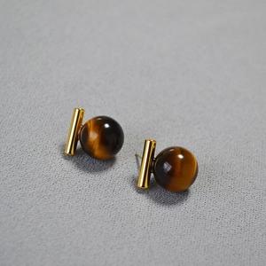 Vue macro des boucles d'oreilles œil de tigre avec cylindres en métal doré minimalistes
