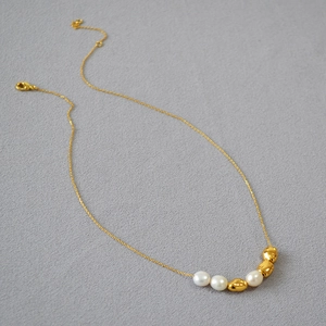 Detail of baroque pearl and gold bead necklace with lobster clasp on grey fabric