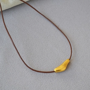 Macro detail of minimalist gold organic pendant with brown leather cord on gray fabric