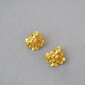 Macro detail of gold-plated stacked floral earrings with matte brushed metal finish