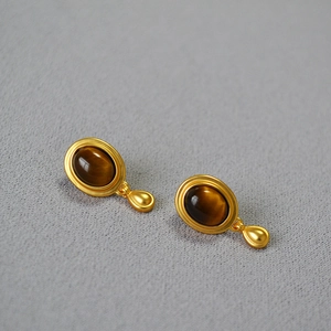 Close-up of vintage matte gold earrings with oval tiger eye stone inlays on grey fabric