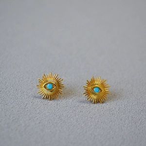 Detail of gold-plated sunburst stud earrings featuring turquoise evil eye in center
