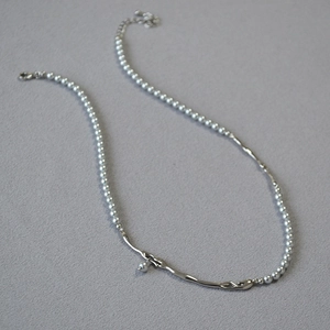 Collier de perles argentées avec pendentif en métal liquide sur tissu gris texturé