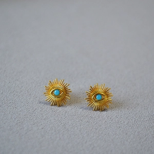 Macro shot of gold-plated evil eye stud earrings with radial texture and turquoise inlay