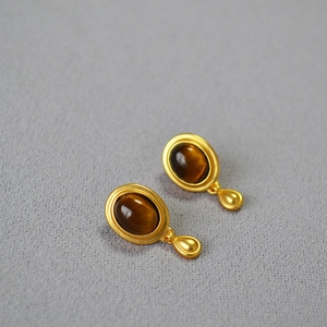 Detail of vintage gold earrings featuring oval tiger eye stone and drop pendant accents