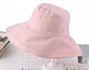 Detailed view of pink sun hat with golden Seek your beauty embroidery on brim