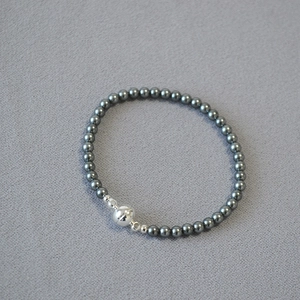 Macro detail of Tahitian faux pearl necklace with silver magnetic clasp on grey fabric