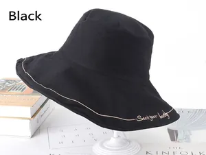 Detail of black cotton bucket hat with beige embroidery and wide brim on a stand