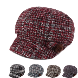 Detailed view of women's tweed octagonal cap featuring red plaid pattern and plush side pom