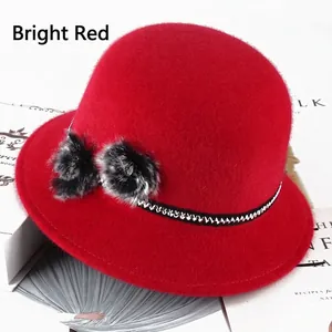 Detail of red cloche hat featuring decorative faux fur pom-poms and geometric band trim