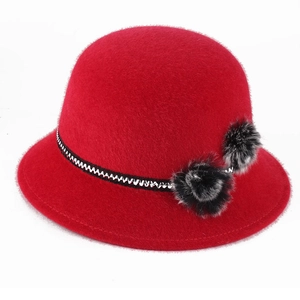 Detail of red faux fur dome hat with black faux fur pom-poms and woven decorative band