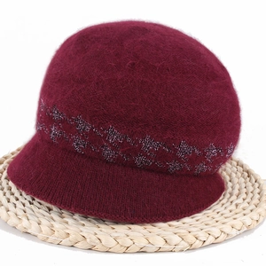 Detailed close-up of burgundy fuzzy winter hat with glitter band on a round woven mat