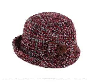 Détail d'un chapeau cloche en tweed rouge et noir avec nœud décoratif et pompon en fourrure