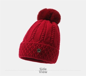 Detailansicht der roten Strickmütze mit Bommel und kleinem Smiley-Metallabzeichen