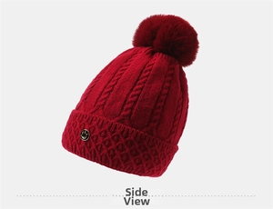 Detail der roten Strickmütze mit Bommel und goldenem Smiley-Emblem für den Winter