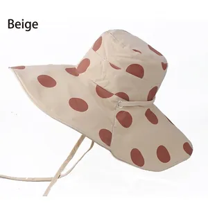 Detail view of the beige sun hat featuring large brown polka dots and a windproof chin strap