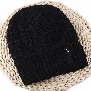 Detailed close-up of a black chunky knit beanie with ribbed cuff on a rustic straw mat