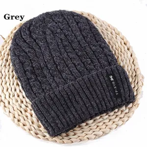 Detail view of grey thick knit beanie with cable pattern and brand label on straw mat