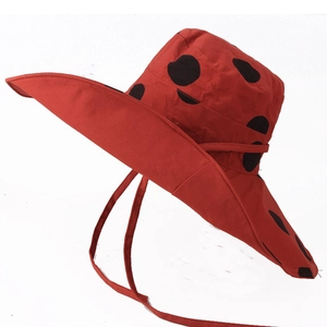 Detailed view of red summer sun hat with large black polka dots and chin strap