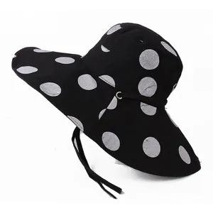 Detail of wide brim sun hat with large white polka dots and adjustable black chin strap