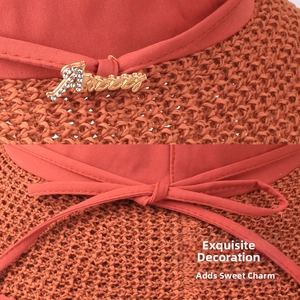 Detail of burnt orange straw sun hat featuring a red bow and gold metal letter accent