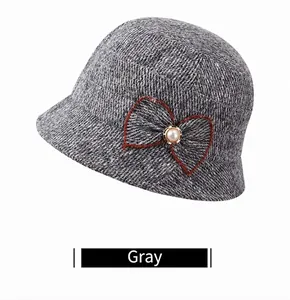 Detail of grey knitted bucket hat featuring a brown bow accent and a white pearl embellishment