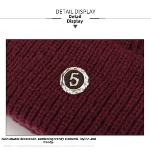 Detailed macro view of a burgundy ribbed knit winter hat with a decorative metal number 5 badge