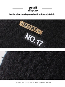 Detail of black teddy fleece fabric with embroidered MORE and NO.17 patches on the hat