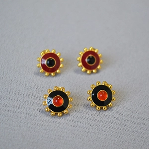 Detail of vintage gold gear earrings with red and black enamel and agate stone inlays