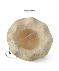 Detail view of woven straw hat featuring wavy brim and adjustable chin strap cord