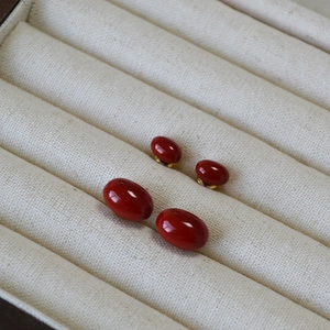 Detailed view of dark red enamel stud earrings with gold base on linen texture background