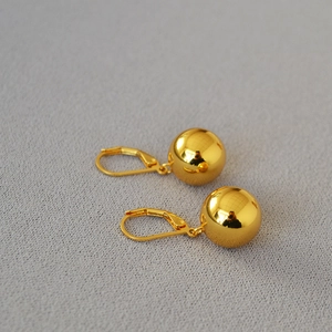 Detailed view of polished hollow gold ball earrings with French lever-back closure