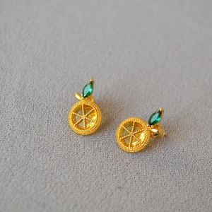 Macro view of lemon-shaped stud earrings featuring yellow gems and green leaf details