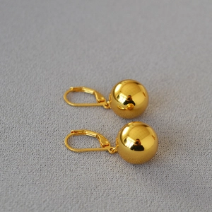 Macro view of French style minimalist hollow gold plated ball earrings on gray fabric