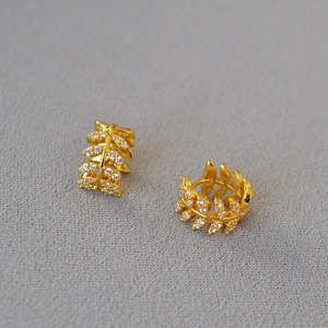 Detailed close-up of golden olive branch earrings with sparkling cubic zirconia inlay