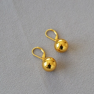Close-up of polished gold-plated hollow ball earrings with hooks on grey textured fabric